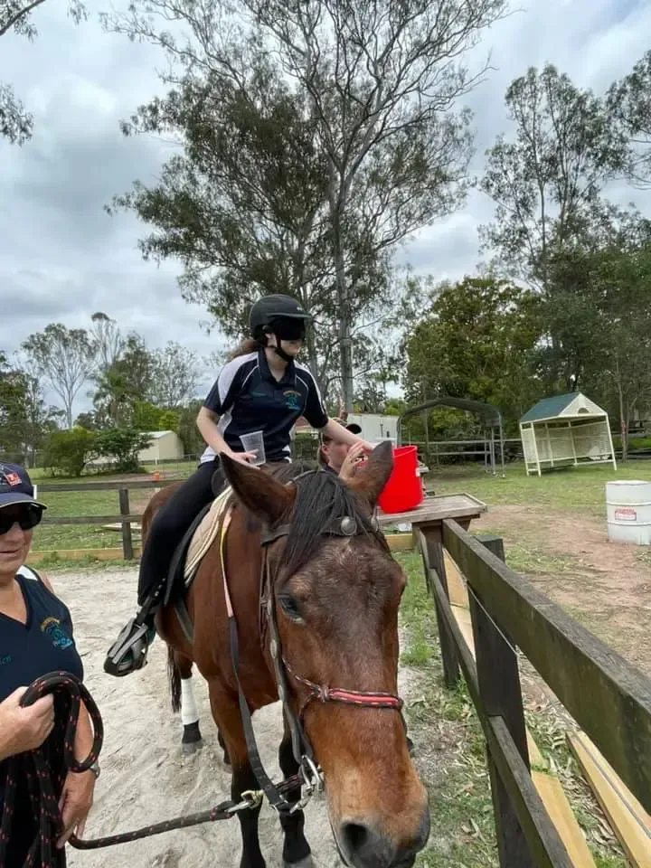 Person on horseback at an outdoor riding area; another person holds a lead rope.