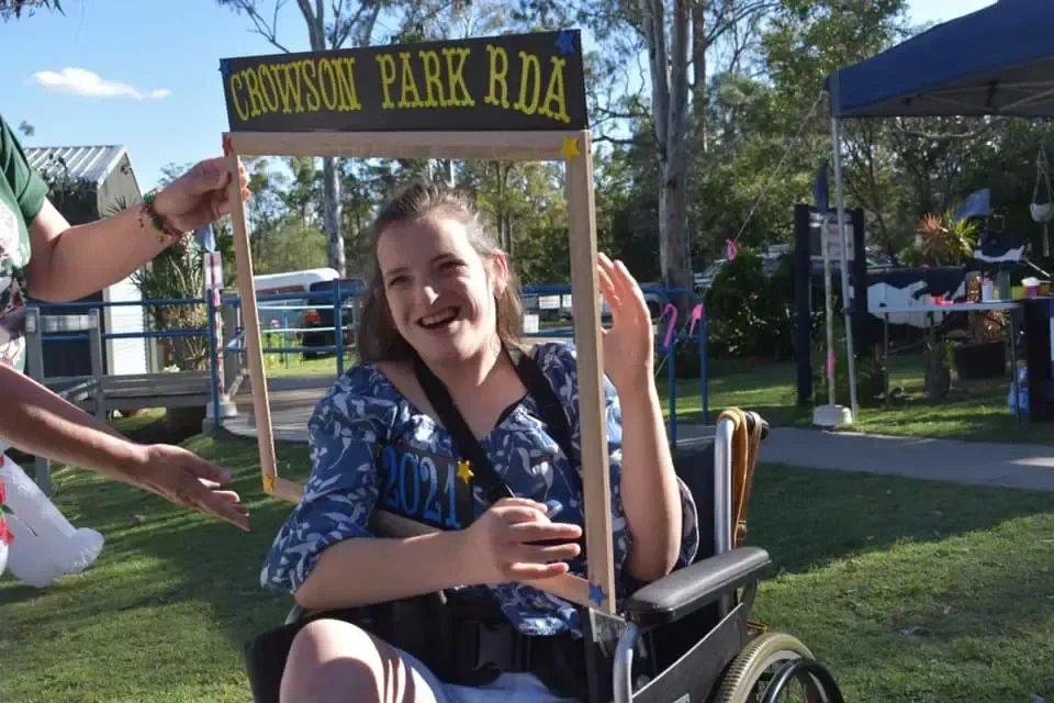 Woman in a wheelchair smiles, holding a sign frame that says