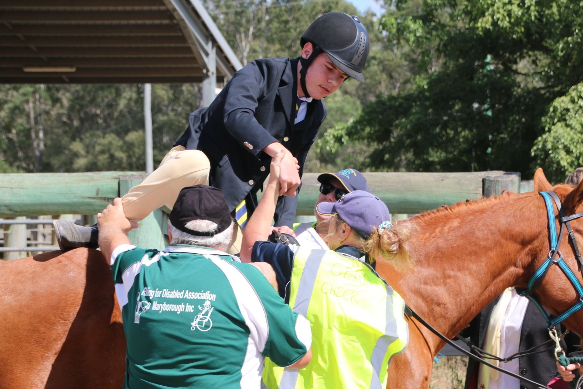 People helping a rider mount a chestnut horse at an outdoor equestrian event.