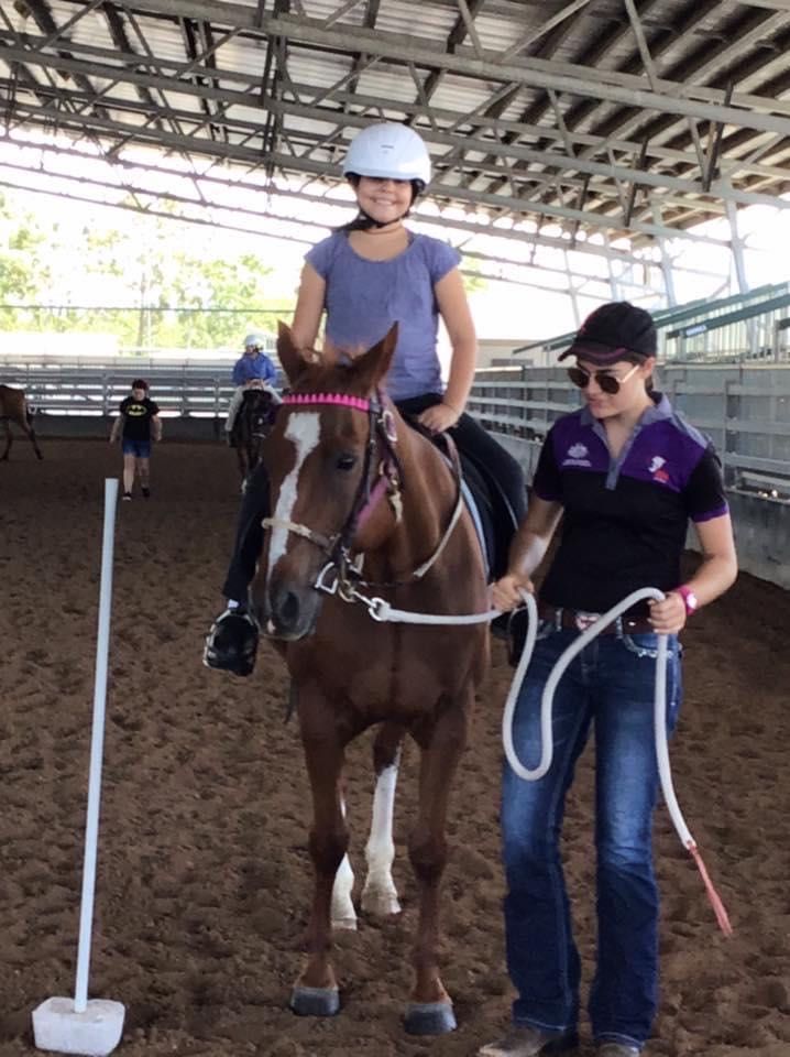 Girl riding a horse, guided by an instructor in a riding arena.