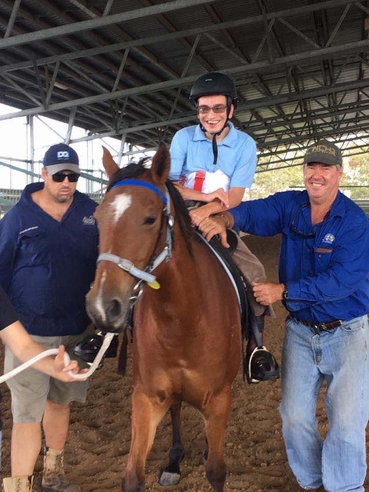 Person riding a brown horse assisted by two people in an indoor arena.