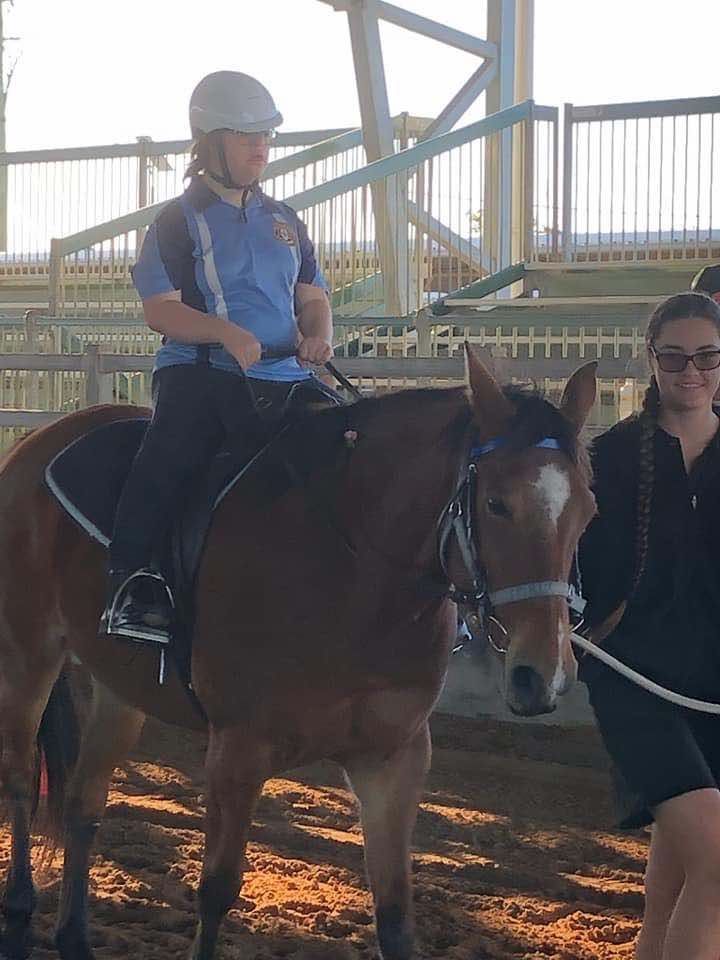 Person riding a brown horse in an indoor arena, another person walks alongside.