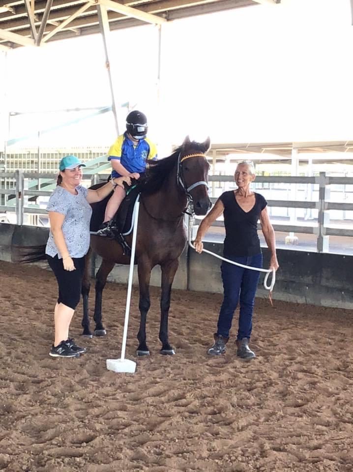 A person wearing a helmet rides a horse, guided by two people in an indoor arena.