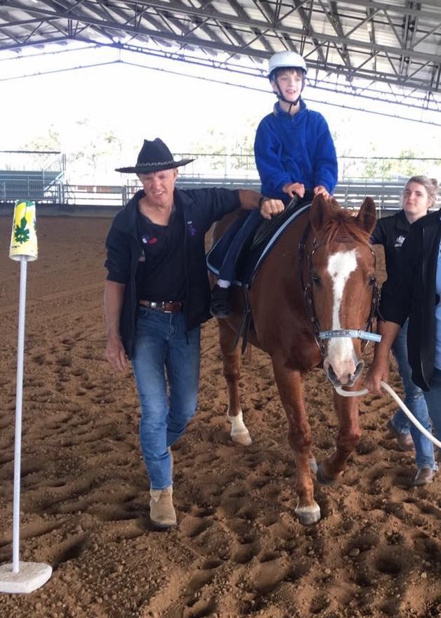 A person on a horse being led by another in a riding arena, a third person is nearby.