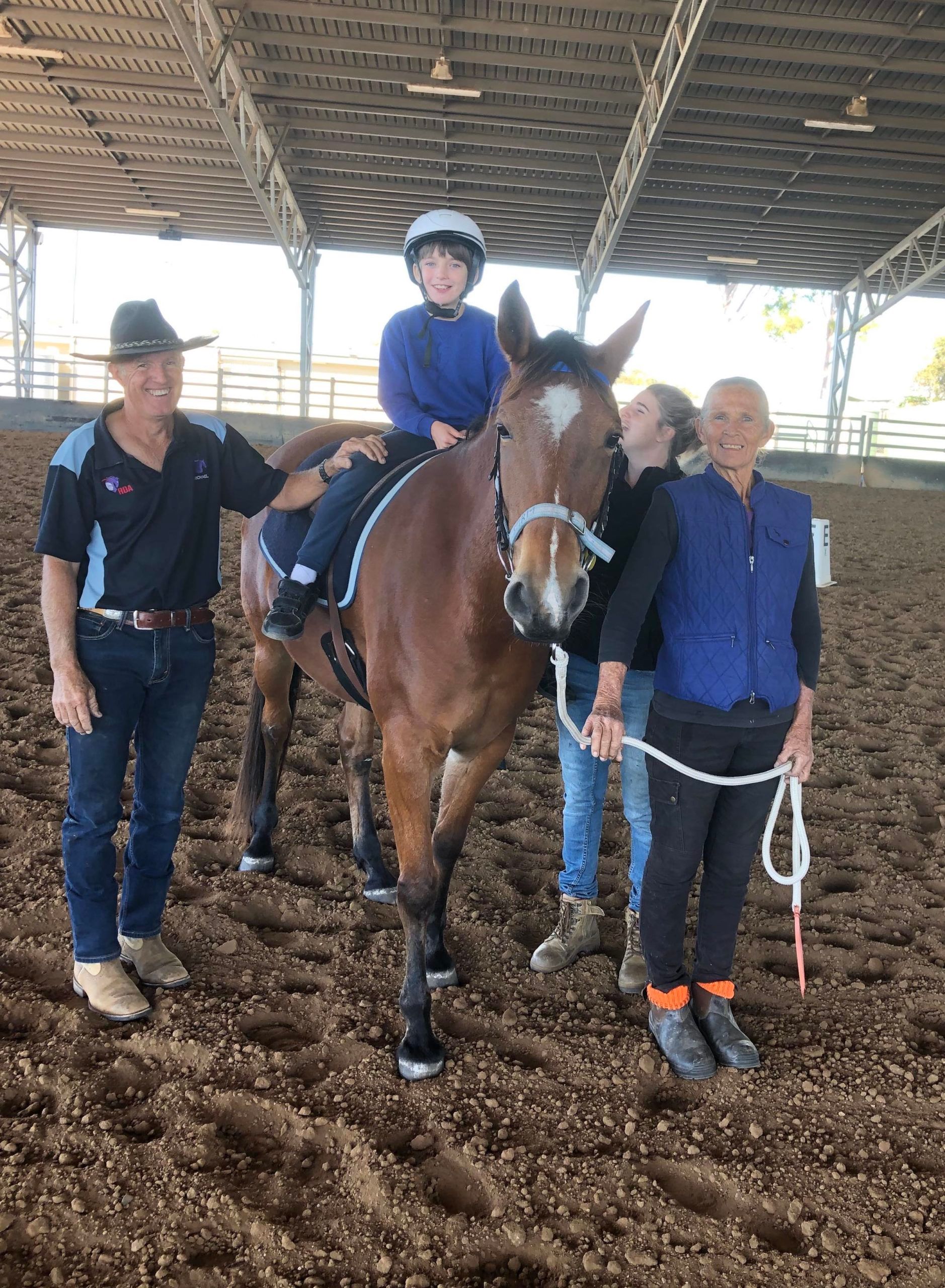 A child on a horse, flanked by adults in an indoor arena.