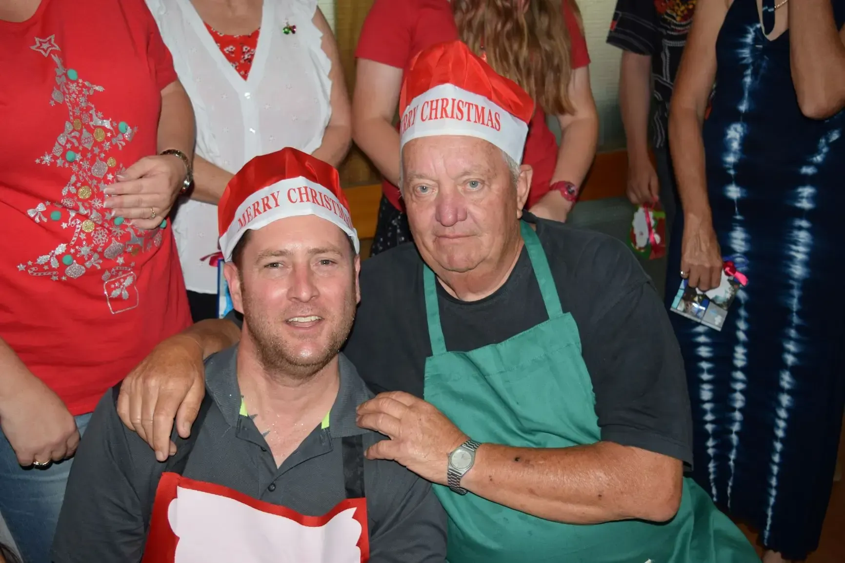 Two men wearing Santa hats and aprons, posing for a photo.