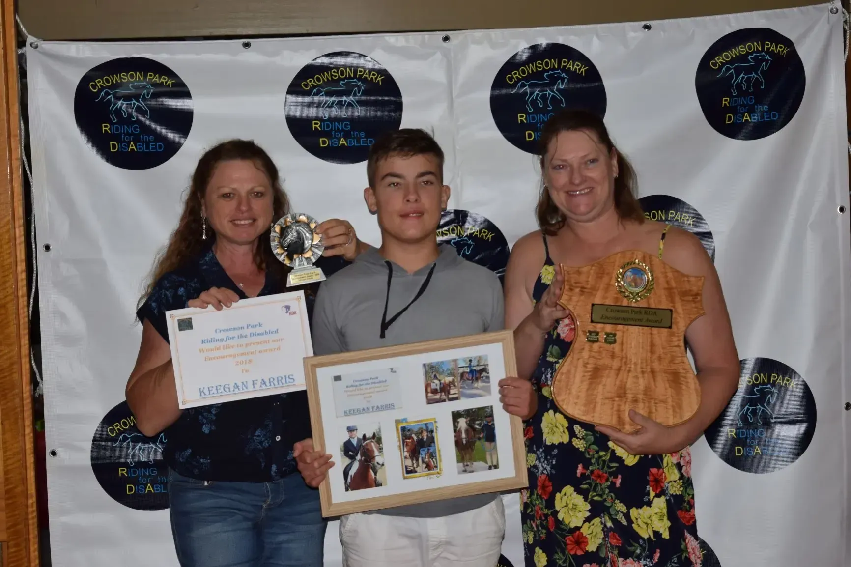 Three people hold awards and pose for a photo in front of a banner.