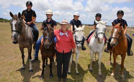 People on horses pose with an instructor on a sunny field.