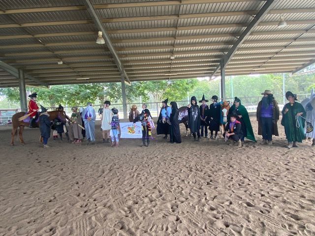 People in costumes with a horse at an equestrian center; a banner is displayed.