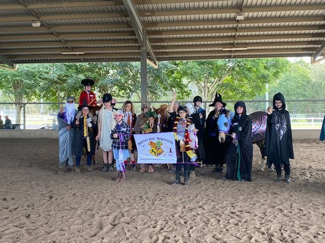 Group dressed in Harry Potter costumes poses with a horse in an arena; banner reads 