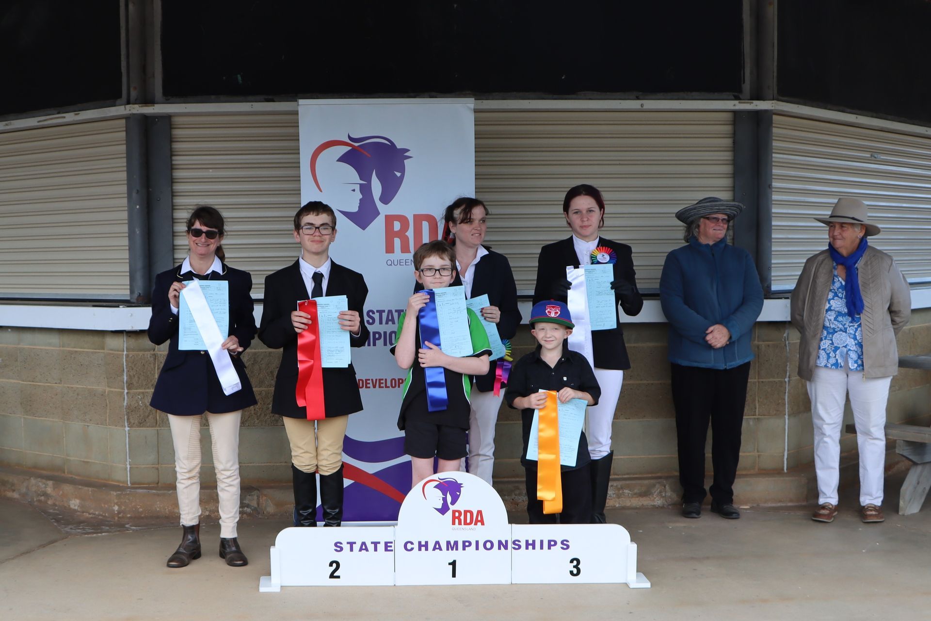 Winners on a podium holding ribbons at a state championships event. A banner in the background.