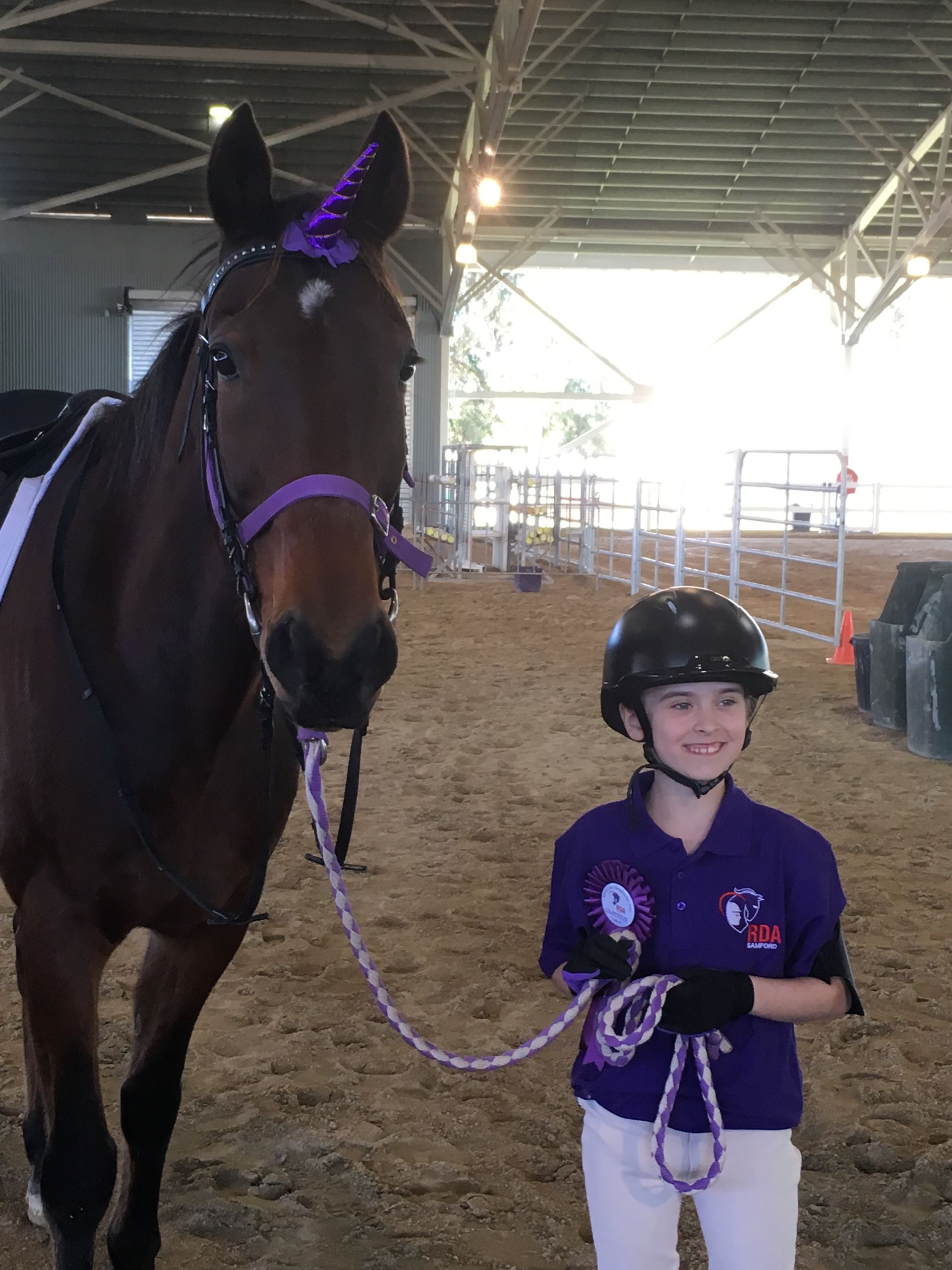A girl in riding gear with a horse decorated as a unicorn, indoors.