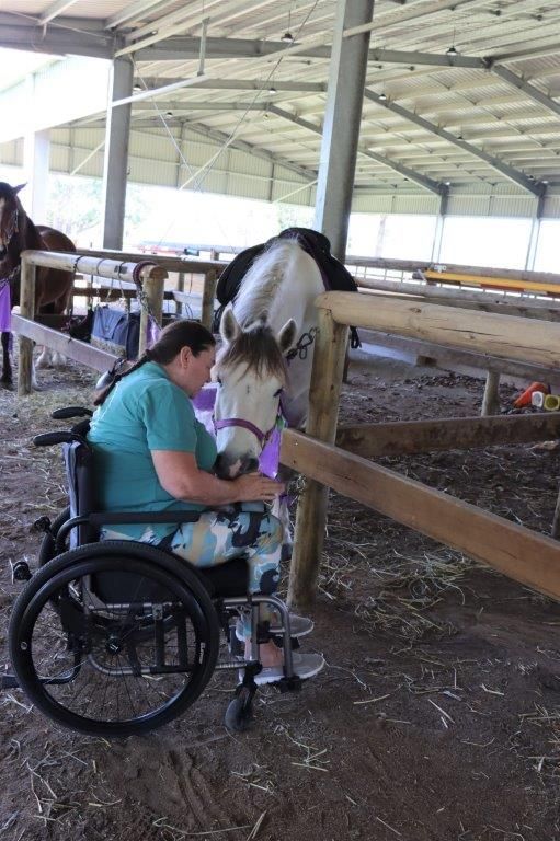 Woman in wheelchair petting a horse at a stable. The horse leans toward the woman.