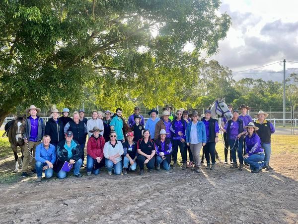 Group of people in purple shirts with horses outdoors.