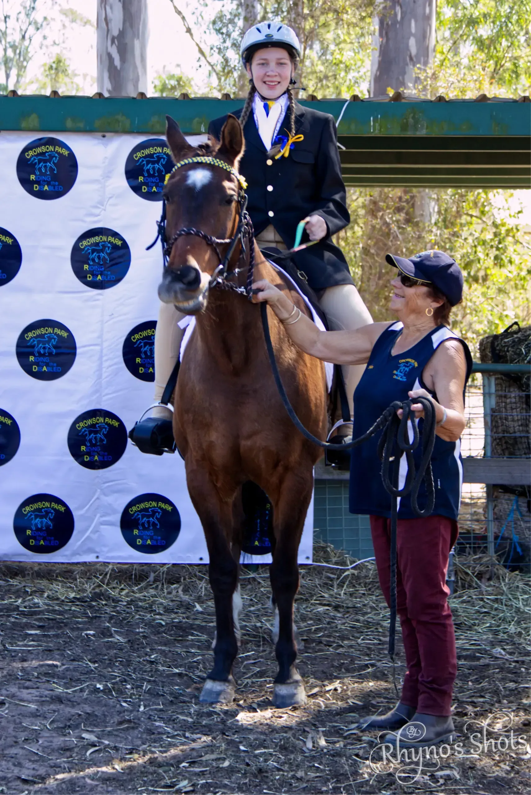 A young equestrian on a horse, with a woman beside them. They are standing near a banner outdoors.