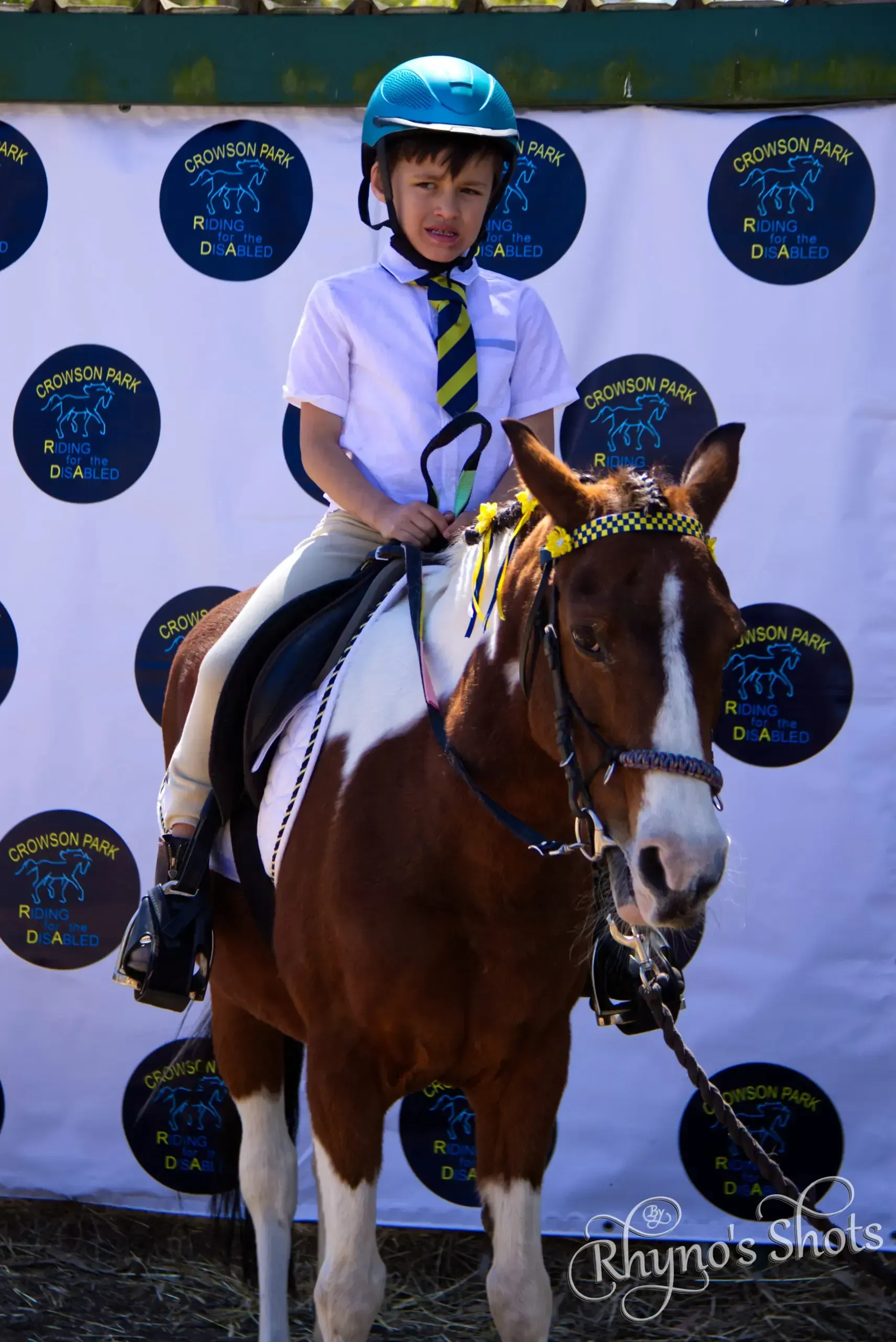 Young person on a brown and white pony, wearing a helmet, at an equestrian event.