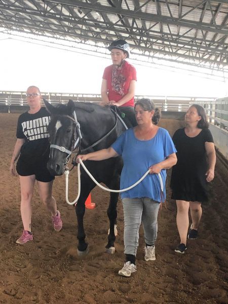 Person riding a horse, guided by three people in an indoor arena.