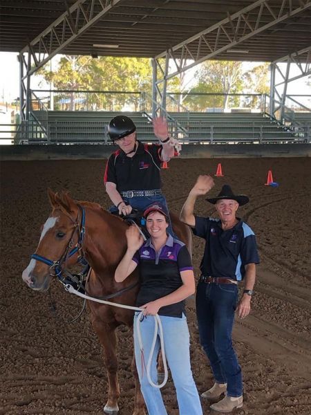 A person on horseback waves, flanked by two people also waving in an arena.