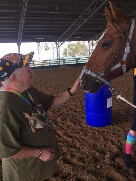 Person petting a brown horse in an indoor arena. The person wears a bandana and green shirt.