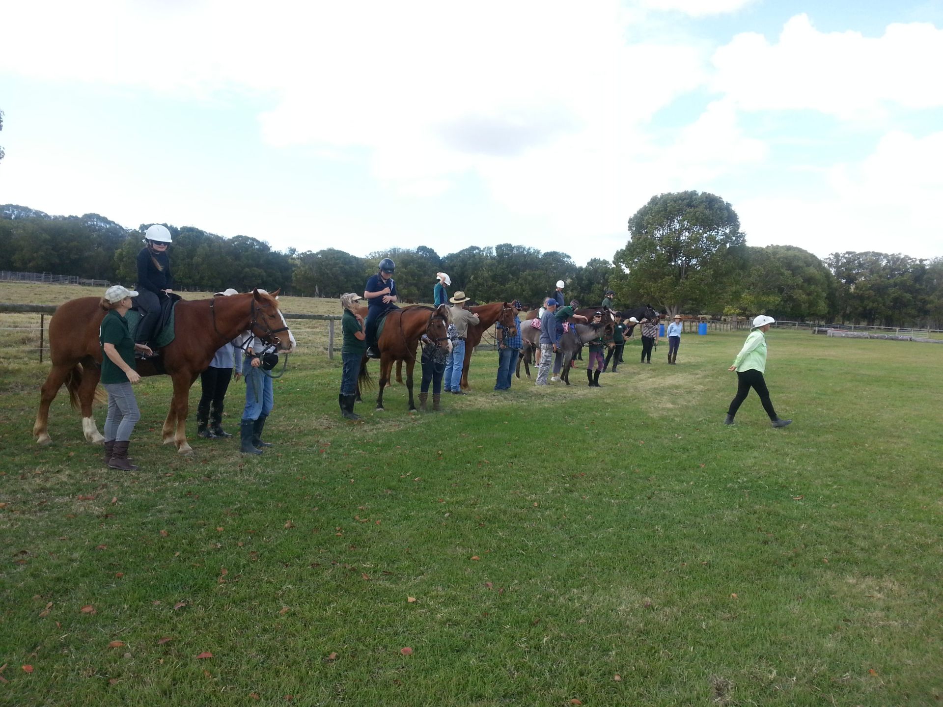 People gather with horses in a grassy field; two riders, others standing with horses.