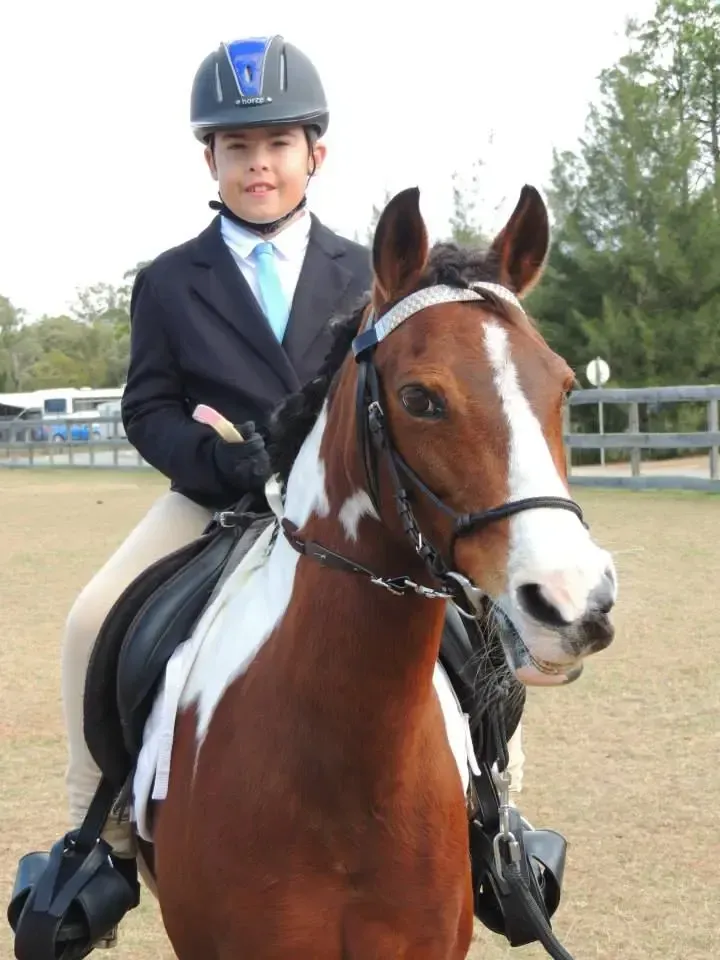 A child in equestrian attire on a brown and white horse, seated in a ring.