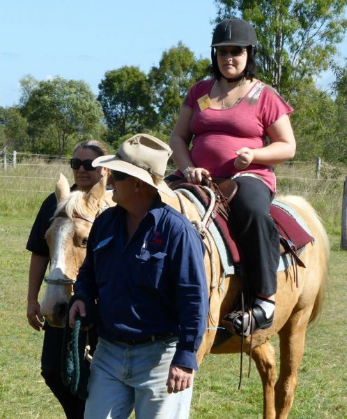 Woman riding a palomino horse, guided by two people in a grassy field.