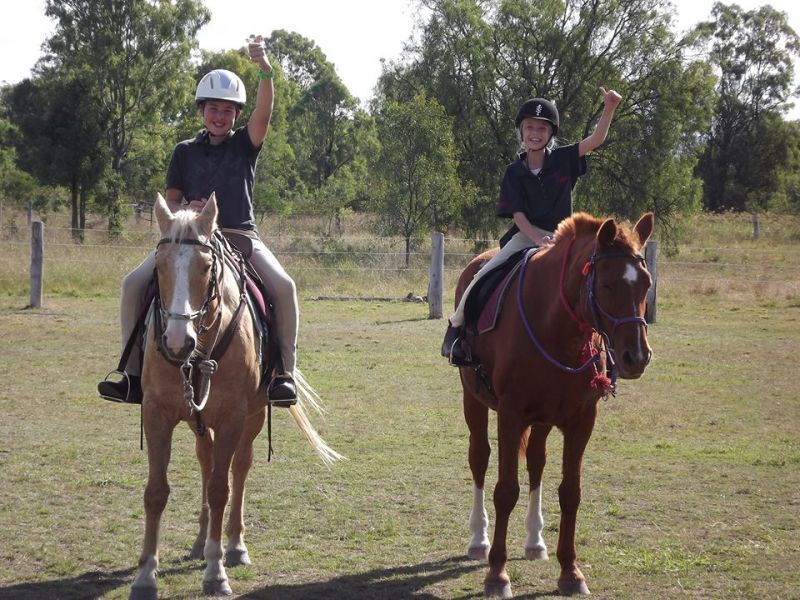 Two riders on horseback, fists raised in the air, outdoors on a grassy field.