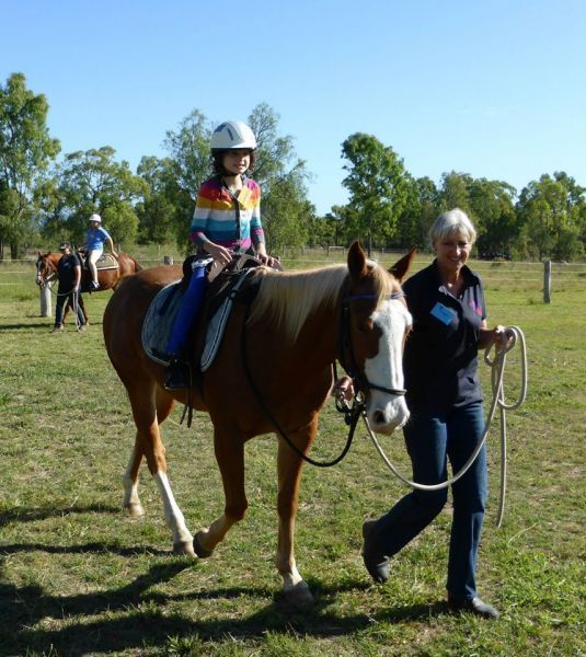 Girl in helmet on horse led by woman in a field.