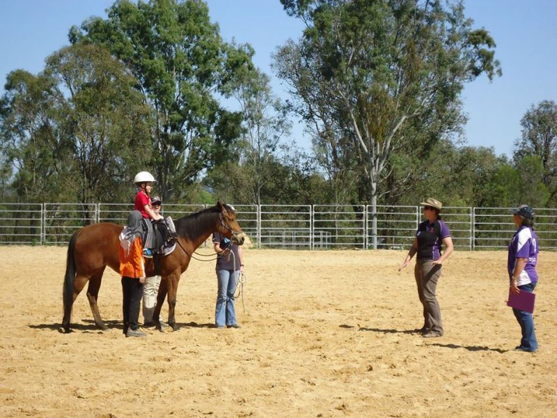 Child on a horse with instructors in an outdoor riding arena.