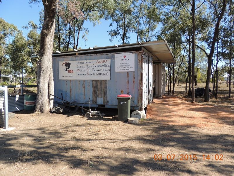 Weathered blue shed with signs, trash can, and dirt path in a wooded area.