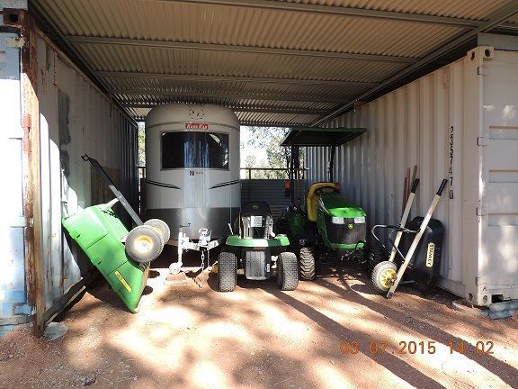 Storage shed with lawn equipment: tractor, trailer, wheelbarrows, and garden machinery.