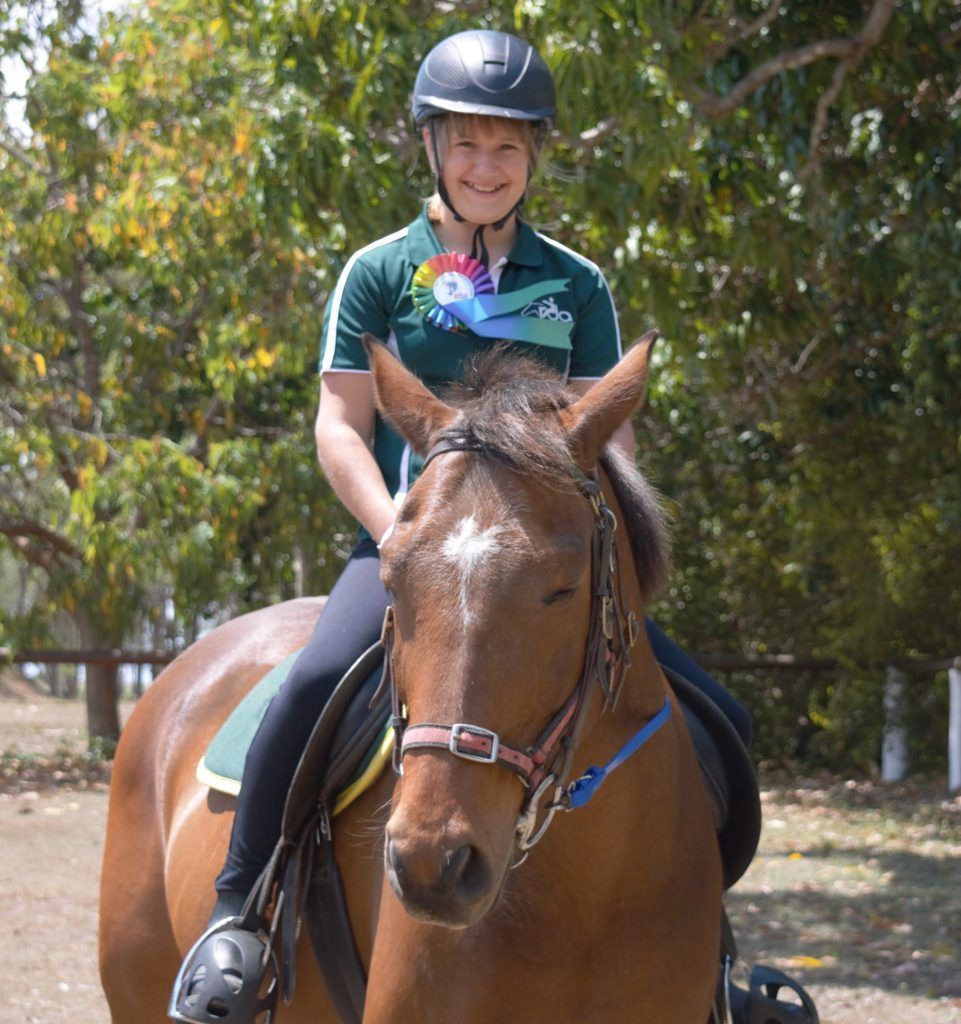 Woman in helmet riding a brown horse; outdoors, blue and green accents.
