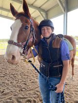 Woman in riding gear with a brown and white horse in a covered arena.