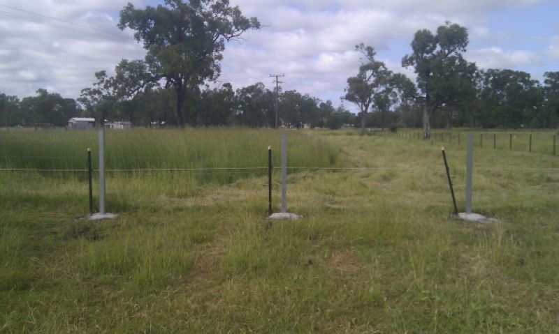 Three gray fence posts set in concrete in a grassy field with trees in the background.