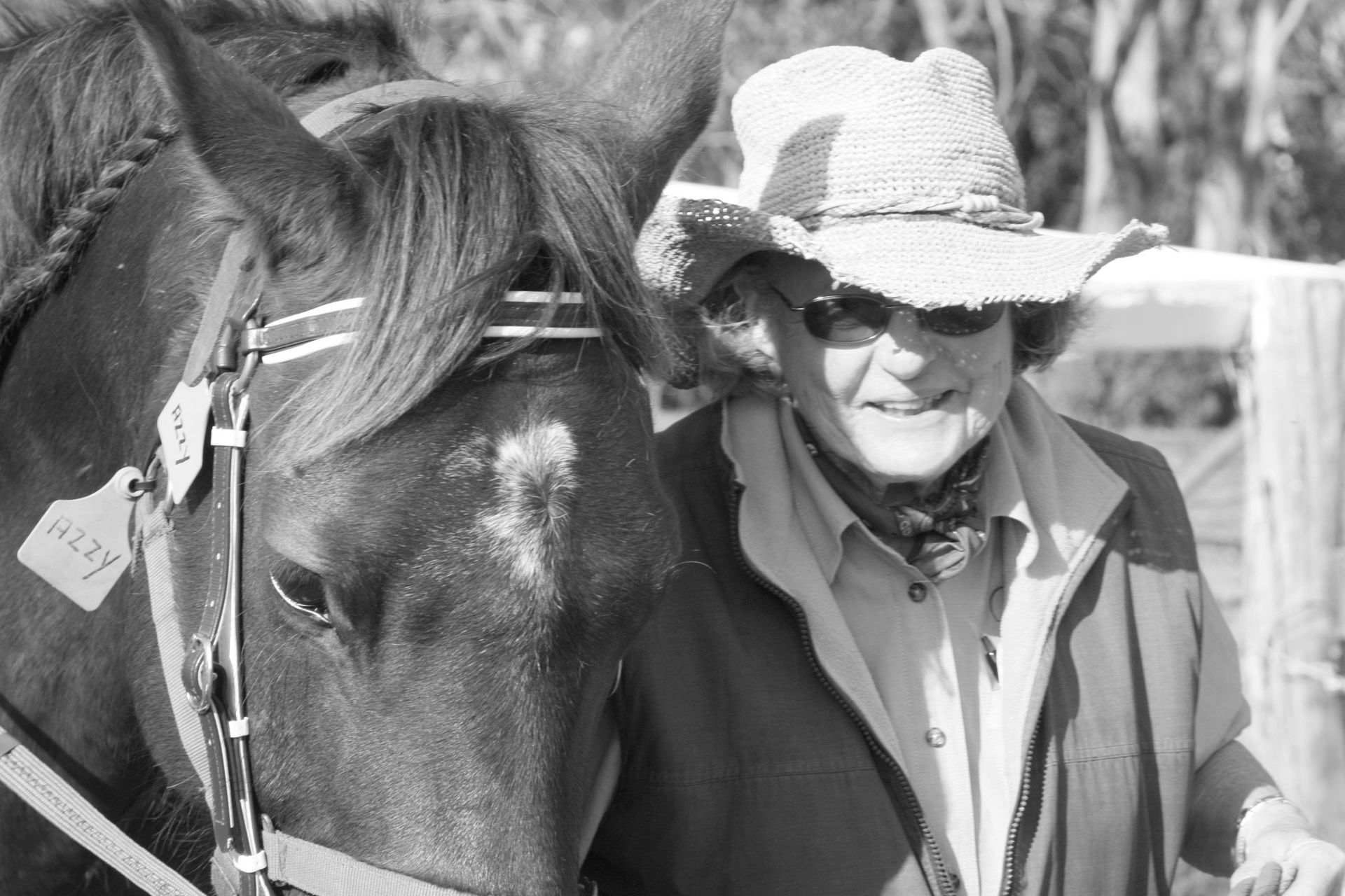 Woman in straw hat smiles next to a horse wearing a bridle.