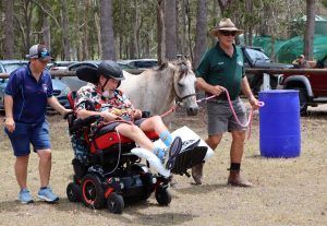 Man in wheelchair with horse, assisted by two people outdoors.