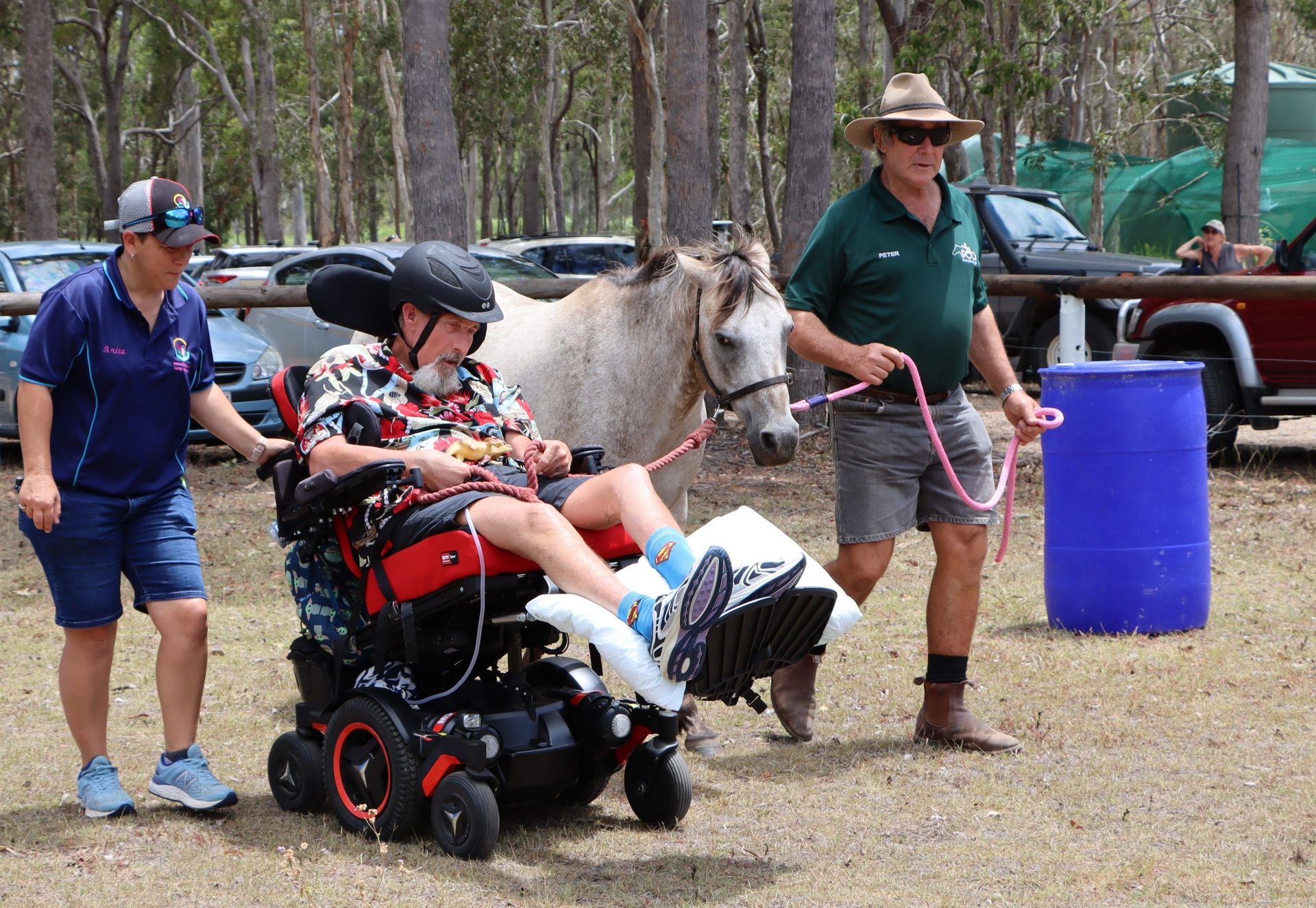 Man in wheelchair with horse, assisted by two people outdoors.