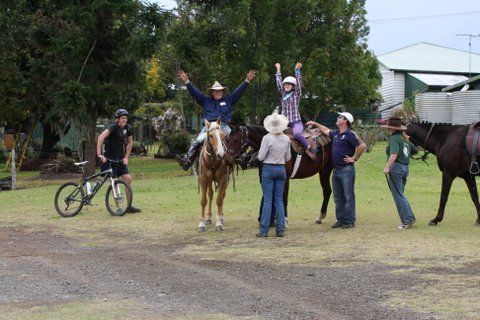 People on horses and ground, cheering; outdoor setting with greenery and buildings.