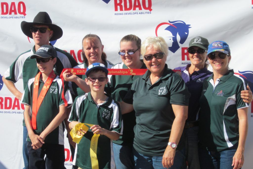 Group of people smiling, holding ribbons, standing in front of a banner with a horse head logo.