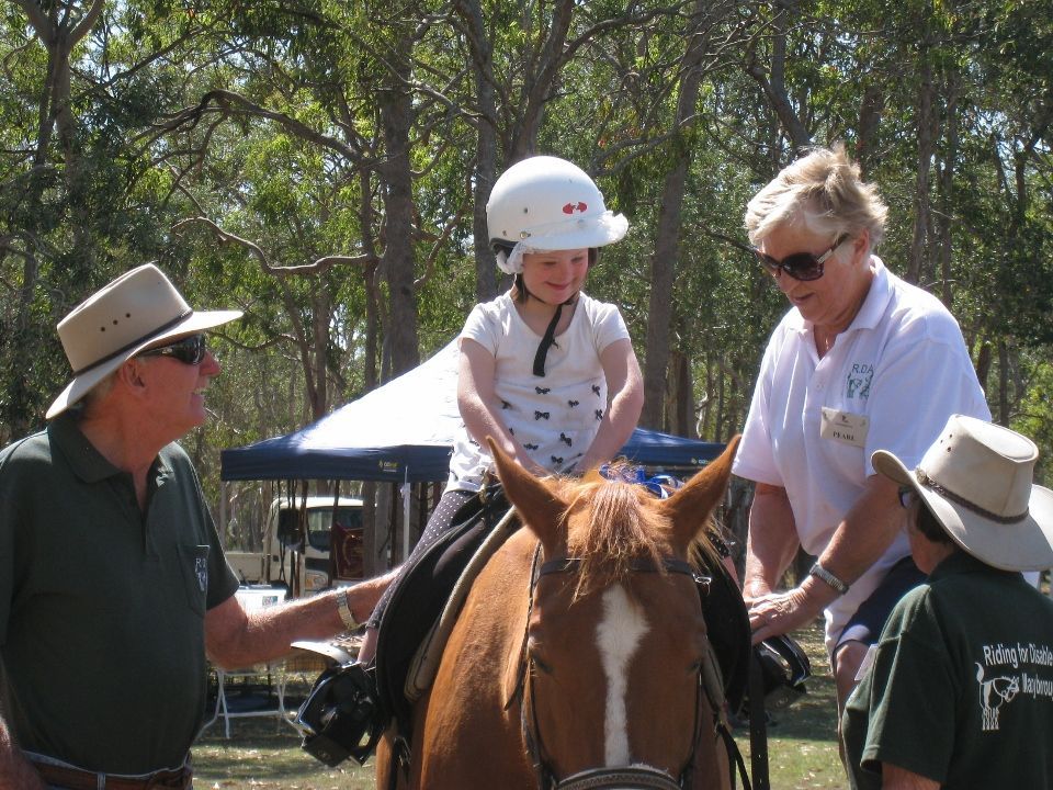 Child on a horse wearing a helmet, supervised by adults outdoors.