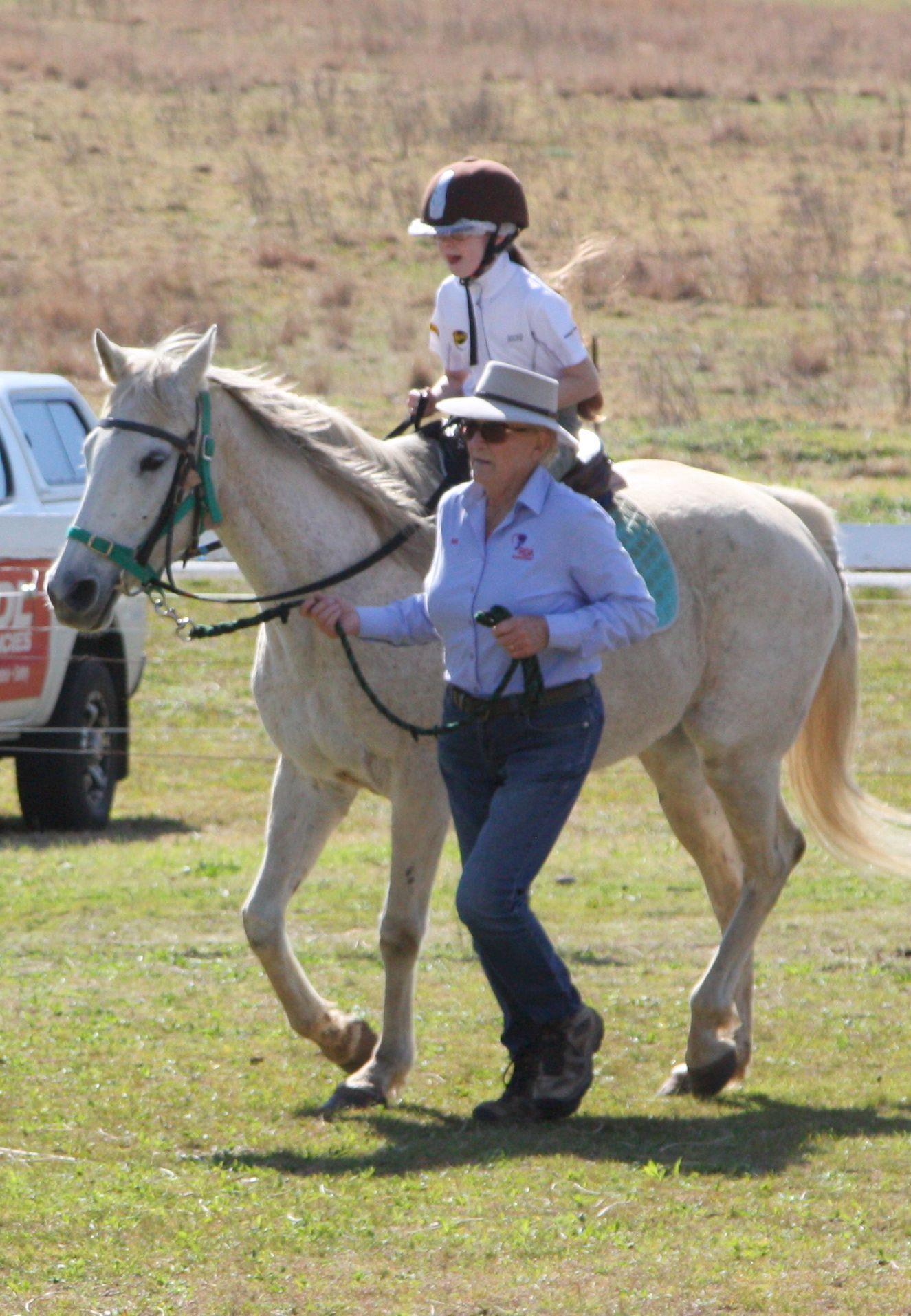 A child riding a palomino horse, led by an adult in a field.