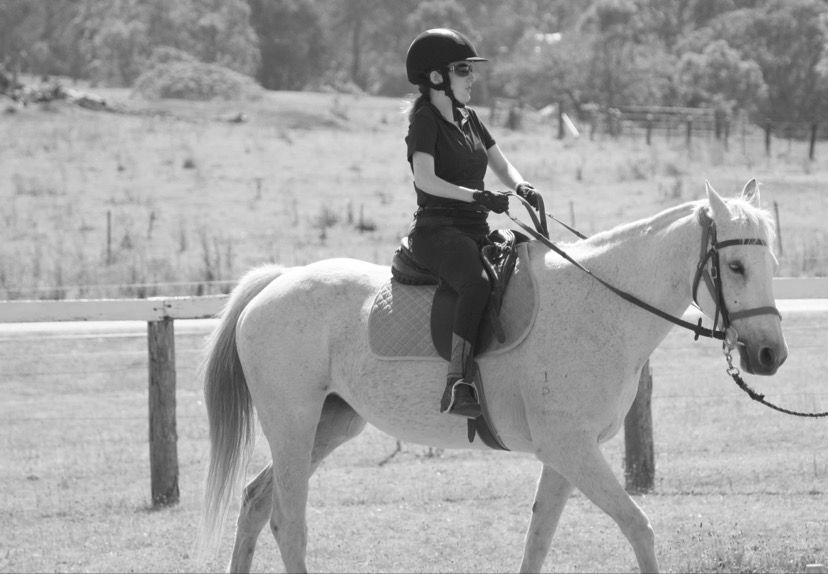 Person riding a white horse in an outdoor field, wearing a helmet and gloves.
