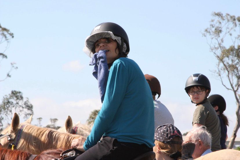 Group of people on horseback outdoors, some wearing helmets and looking at the camera.