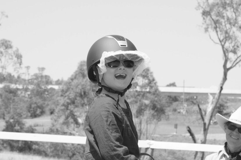Child wearing a riding helmet with a sun visor and sunglasses, smiling.