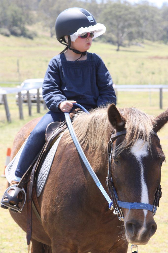 Child on a brown horse wearing a helmet and sunglasses; outdoors.