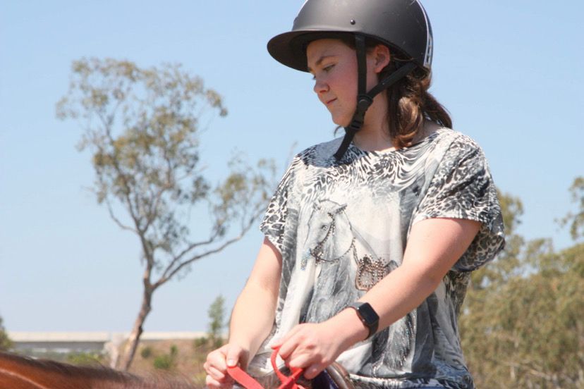 Person in helmet holding reins, outdoors, preparing to ride a horse on a sunny day.