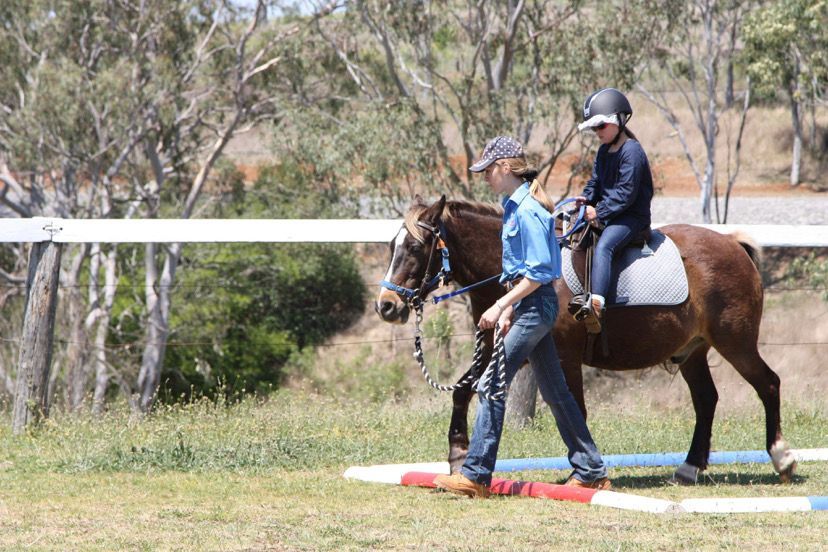 A person leading a horse with a rider along a red and white path in an outdoor setting.
