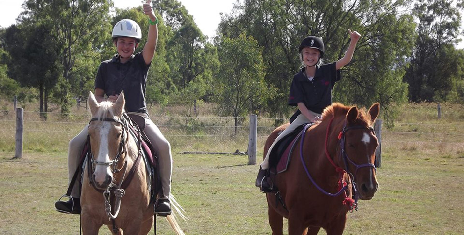 Two people on horseback raise their arms in a field, celebrating.