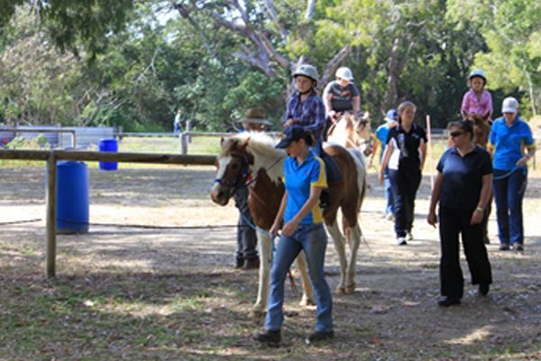 People riding ponies outdoors, led by instructors.