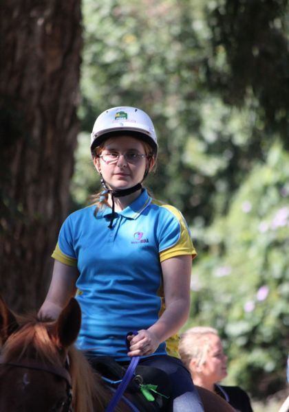 Person in riding helmet and blue shirt on a horse outdoors.